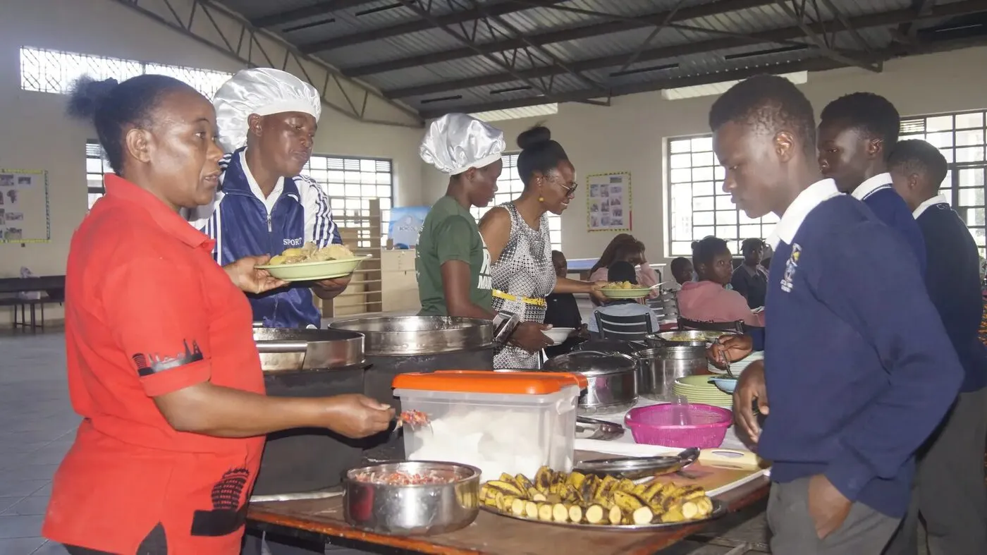 Kitchen staff serving hot meals to pupils in line